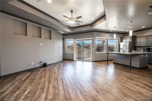 kitchen with hanging light fixtures, stainless steel refrigerator with ice dispenser, a tray ceiling, a kitchen bar, and a center island with sink