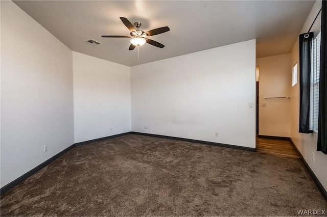 spare room featuring a ceiling fan, dark colored carpet, visible vents, and baseboards