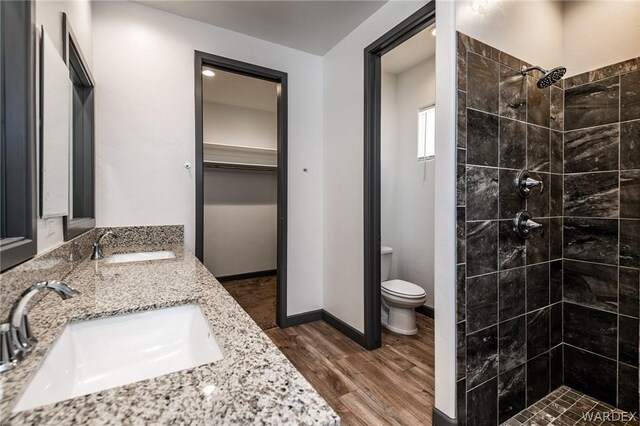 bathroom featuring toilet, a spacious closet, a sink, and wood finished floors