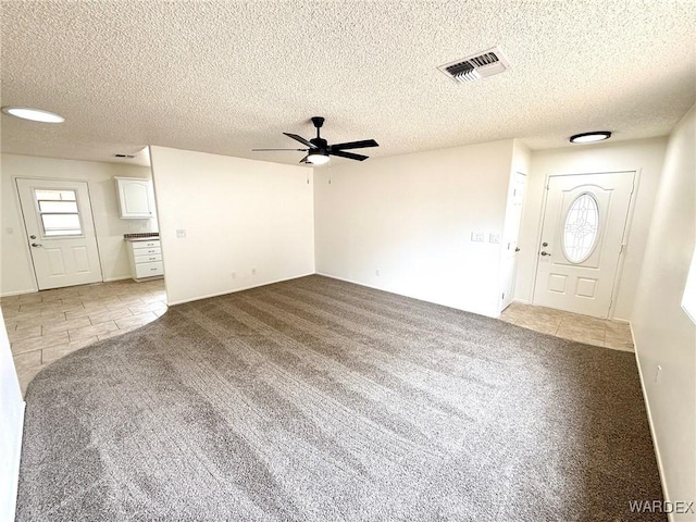 foyer entrance with light carpet, ceiling fan, visible vents, and a textured ceiling