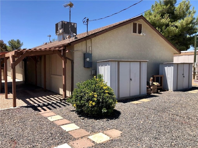 view of home's exterior featuring stucco siding, an outdoor structure, a storage shed, and central air condition unit