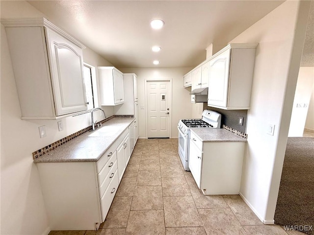 kitchen with light countertops, white cabinetry, a sink, and gas range gas stove