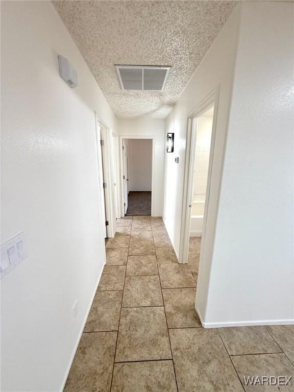 hallway featuring visible vents, a textured ceiling, baseboards, and light tile patterned floors