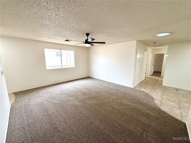 spare room featuring light carpet, light tile patterned floors, visible vents, ceiling fan, and a textured ceiling