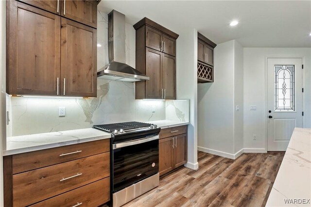 10726 S River Terrace Dr, Mohave Valley, AZ 86440 - kitchen with wall chimney range hood, stainless steel range with gas stovetop, light wood-style flooring, light stone counters, and decorative backsplash
