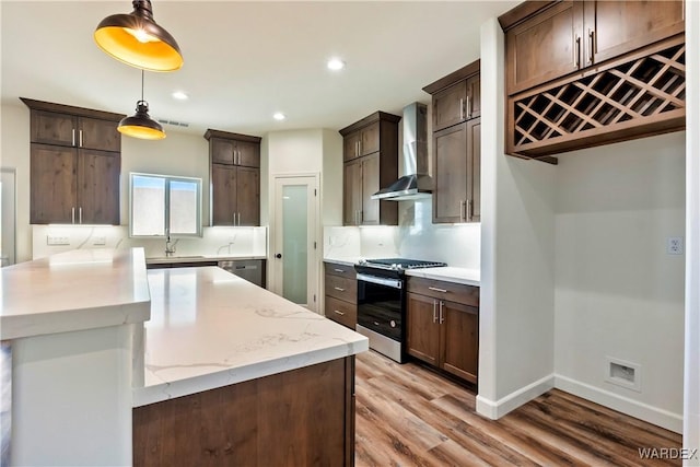 10726 S River Terrace Dr, Mohave Valley, AZ 86440 - kitchen featuring stainless steel gas range oven, wall chimney exhaust hood, dark brown cabinets, light wood-type flooring, and decorative light fixtures