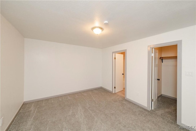 unfurnished bedroom featuring light carpet, a spacious closet, a textured ceiling, and baseboards