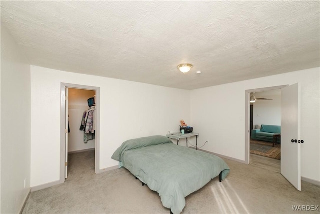 bedroom with baseboards, a walk in closet, and light colored carpet