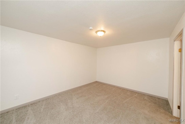 empty room with light carpet, a textured ceiling, and baseboards