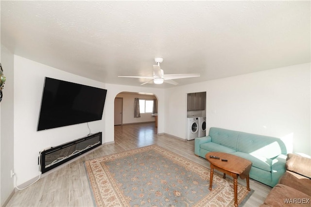 living room featuring arched walkways, light wood-style flooring, ceiling fan, a textured ceiling, and separate washer and dryer