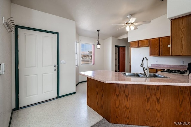 kitchen featuring brown cabinets, a peninsula, light countertops, light floors, and a sink