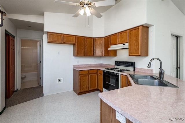 kitchen featuring brown cabinets, gas stove, a sink, and under cabinet range hood