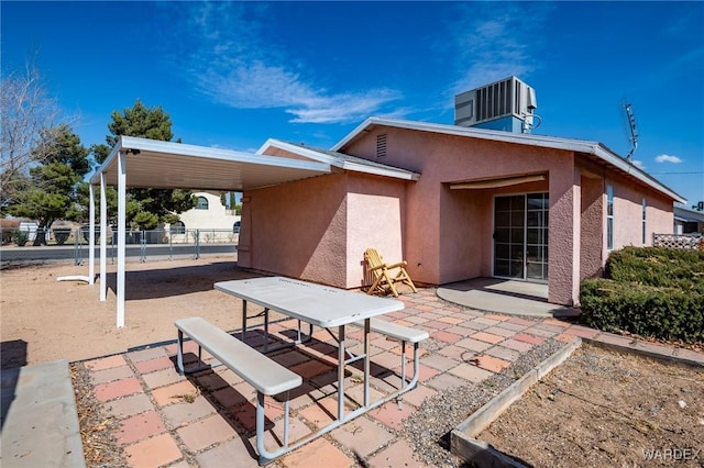 rear view of house featuring an attached carport, cooling unit, fence, stucco siding, and a patio area