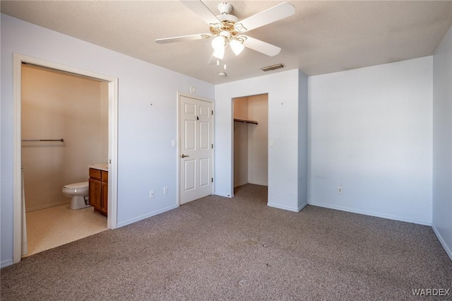 unfurnished bedroom featuring ensuite bathroom, light carpet, a ceiling fan, baseboards, and visible vents