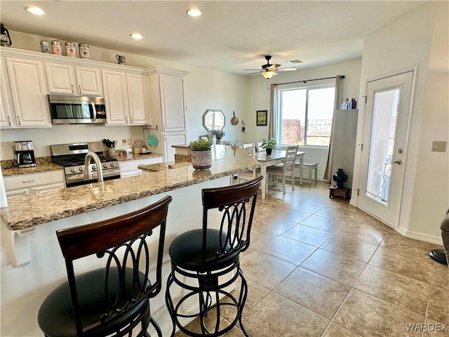 kitchen with recessed lighting, a ceiling fan, stainless steel appliances, and a kitchen bar