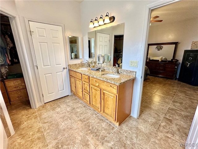 bathroom with a walk in closet, double vanity, a sink, and a ceiling fan