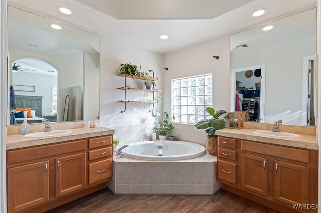 ensuite bathroom featuring ensuite bath, a walk in closet, a sink, and wood finished floors