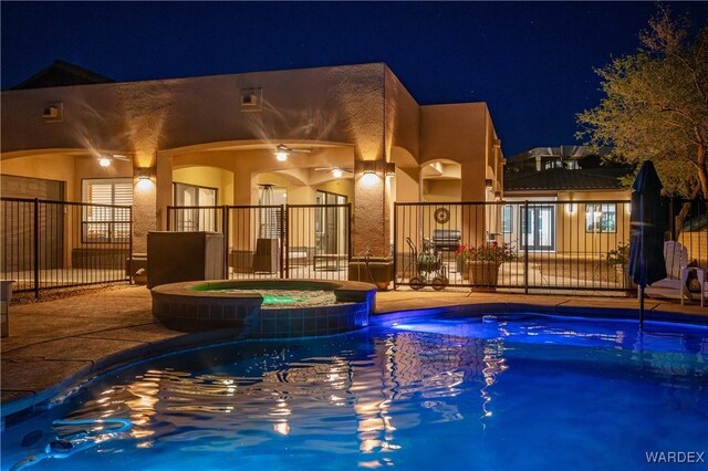 back of house at twilight featuring a pool with connected hot tub, stucco siding, fence, and a patio