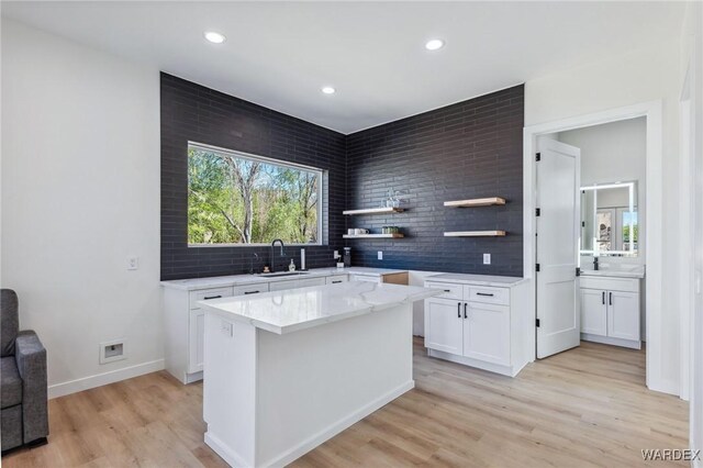 kitchen with light wood finished floors, open shelves, white cabinets, a kitchen island, and a sink