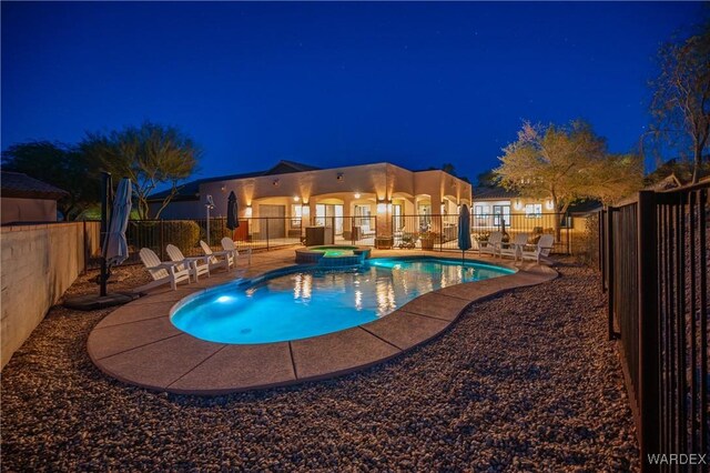 pool at night with a patio area, a fenced backyard, and a pool with connected hot tub