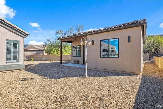 rear view of house with a tiled roof, a patio area, fence, and stucco siding