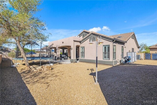 exterior space featuring a trampoline, stucco siding, a patio area, fence, and a tiled roof