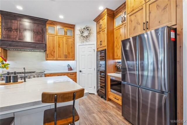 kitchen featuring decorative backsplash, light wood-style flooring, glass insert cabinets, freestanding refrigerator, and light stone countertops