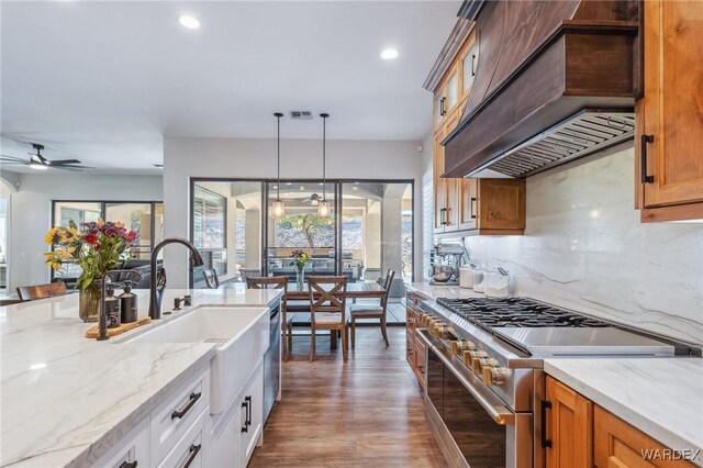 kitchen with pendant lighting, stainless steel appliances, white cabinets, light stone countertops, and custom range hood