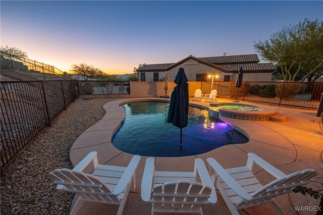 pool at dusk featuring a patio area, a fenced backyard, and a pool with connected hot tub