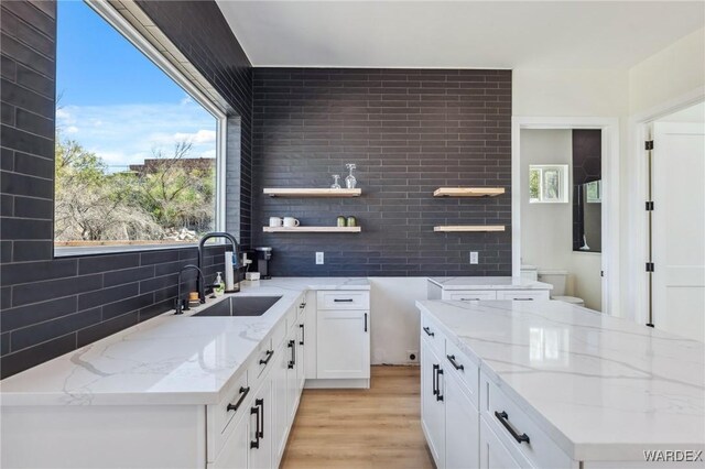 kitchen featuring light stone counters, white cabinets, a sink, and open shelves