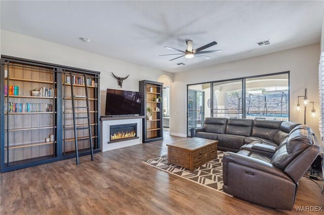 living area featuring ceiling fan, wood finished floors, visible vents, baseboards, and a glass covered fireplace