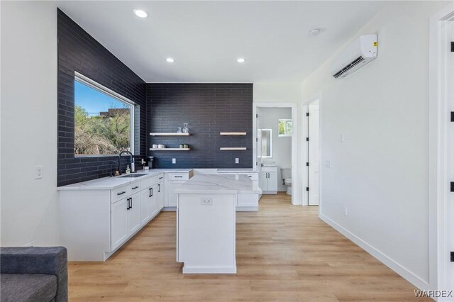 kitchen with tasteful backsplash, white cabinets, a wall mounted air conditioner, a center island, and a sink