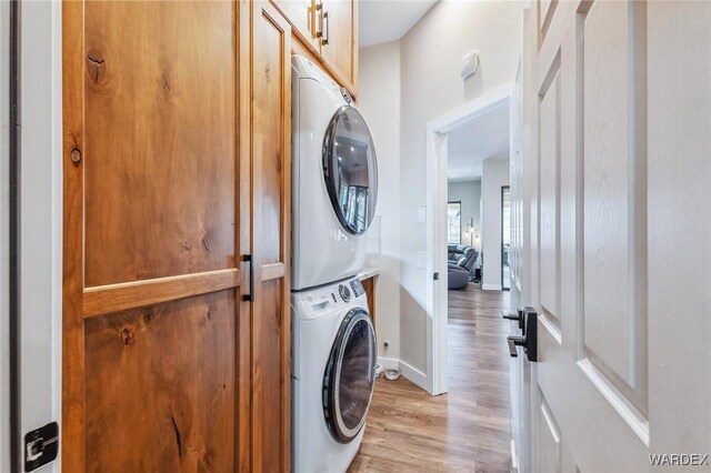 laundry area featuring light wood-type flooring, baseboards, cabinet space, and stacked washing maching and dryer