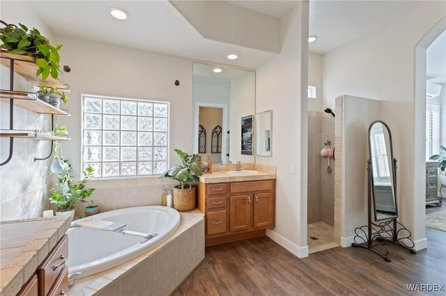 bathroom with wood finished floors, a garden tub, a tile shower, vanity, and recessed lighting