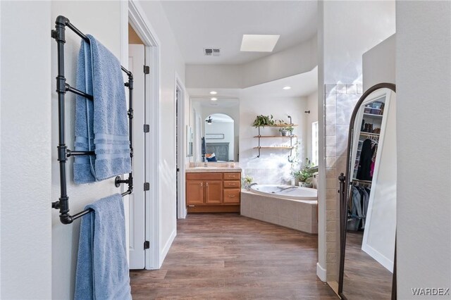 full bath featuring a garden tub, visible vents, a spacious closet, vanity, and wood finished floors