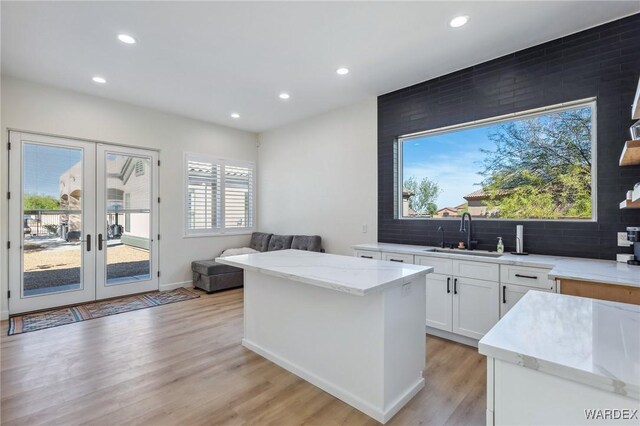 kitchen featuring a sink, a kitchen island, light wood-style floors, white cabinets, and tasteful backsplash