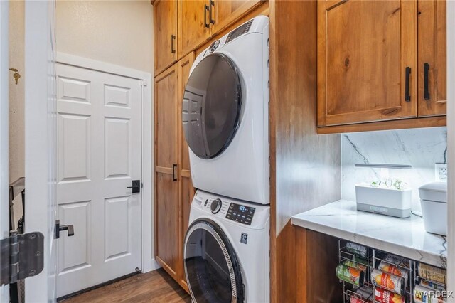 washroom with stacked washer and dryer, dark wood finished floors, and cabinet space