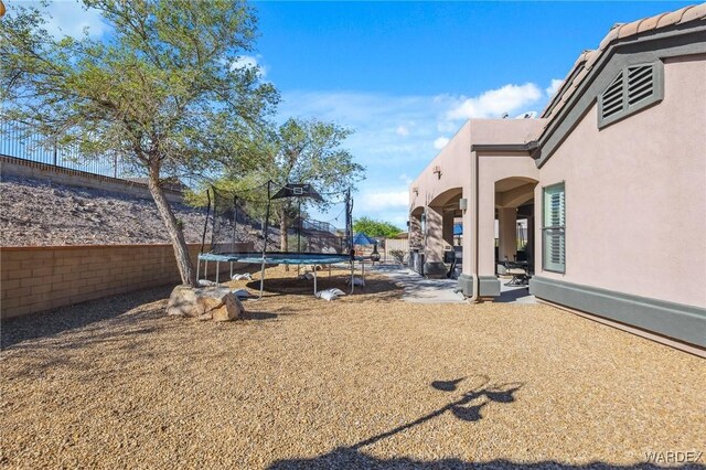 view of yard featuring a trampoline, a patio area, and a fenced backyard