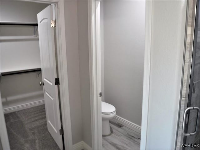 bathroom featuring toilet, baseboards, and a spacious closet
