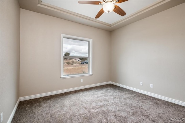 empty room with a raised ceiling, ceiling fan, baseboards, and carpet floors