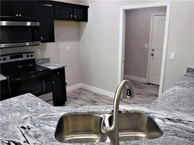 kitchen with baseboards, a sink, appliances with stainless steel finishes, dark cabinetry, and light wood-style flooring