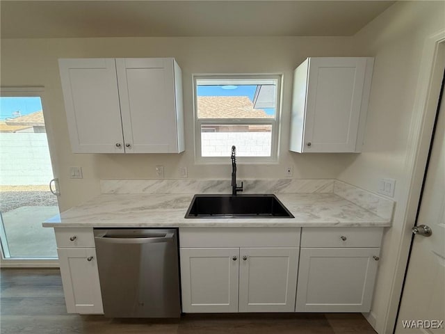 kitchen with a sink, white cabinetry, stainless steel dishwasher, light stone countertops, and dark wood finished floors