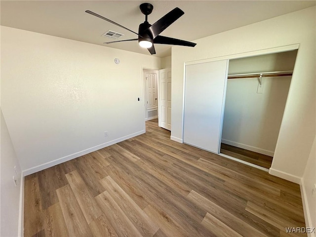 unfurnished bedroom with a closet, visible vents, baseboards, and wood finished floors