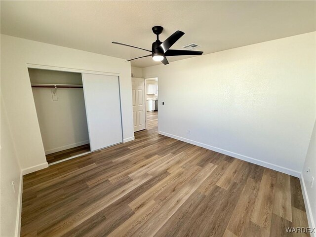 unfurnished bedroom featuring a closet, visible vents, a ceiling fan, wood finished floors, and baseboards