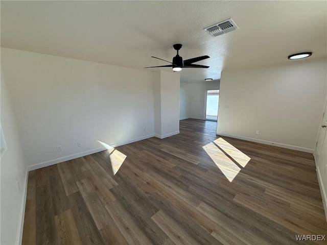 empty room with dark wood-style flooring, visible vents, ceiling fan, and baseboards