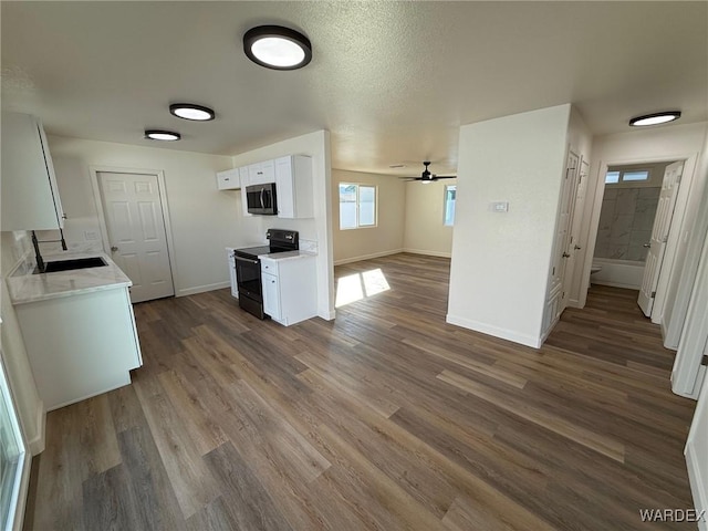 kitchen with dark wood finished floors, stainless steel microwave, light countertops, black electric range, and white cabinetry