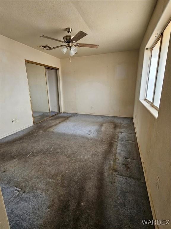 unfurnished bedroom featuring dark colored carpet, a closet, visible vents, a ceiling fan, and a textured ceiling