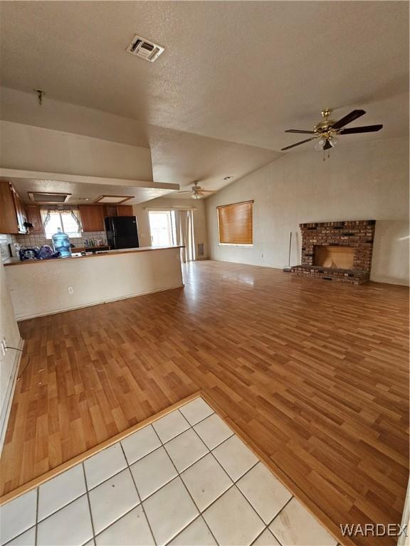 unfurnished living room featuring visible vents, ceiling fan, light wood-style flooring, a brick fireplace, and a wealth of natural light