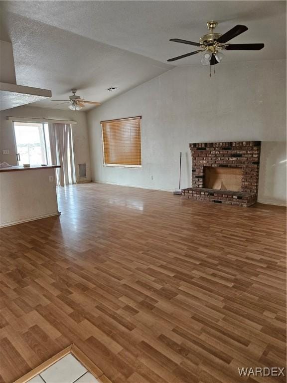 unfurnished living room featuring a ceiling fan, lofted ceiling, wood finished floors, a textured ceiling, and a brick fireplace