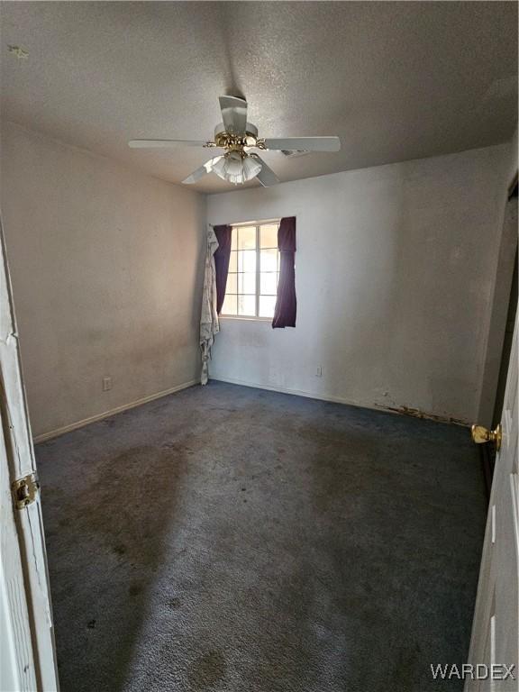 unfurnished room with a textured ceiling, dark colored carpet, and a ceiling fan